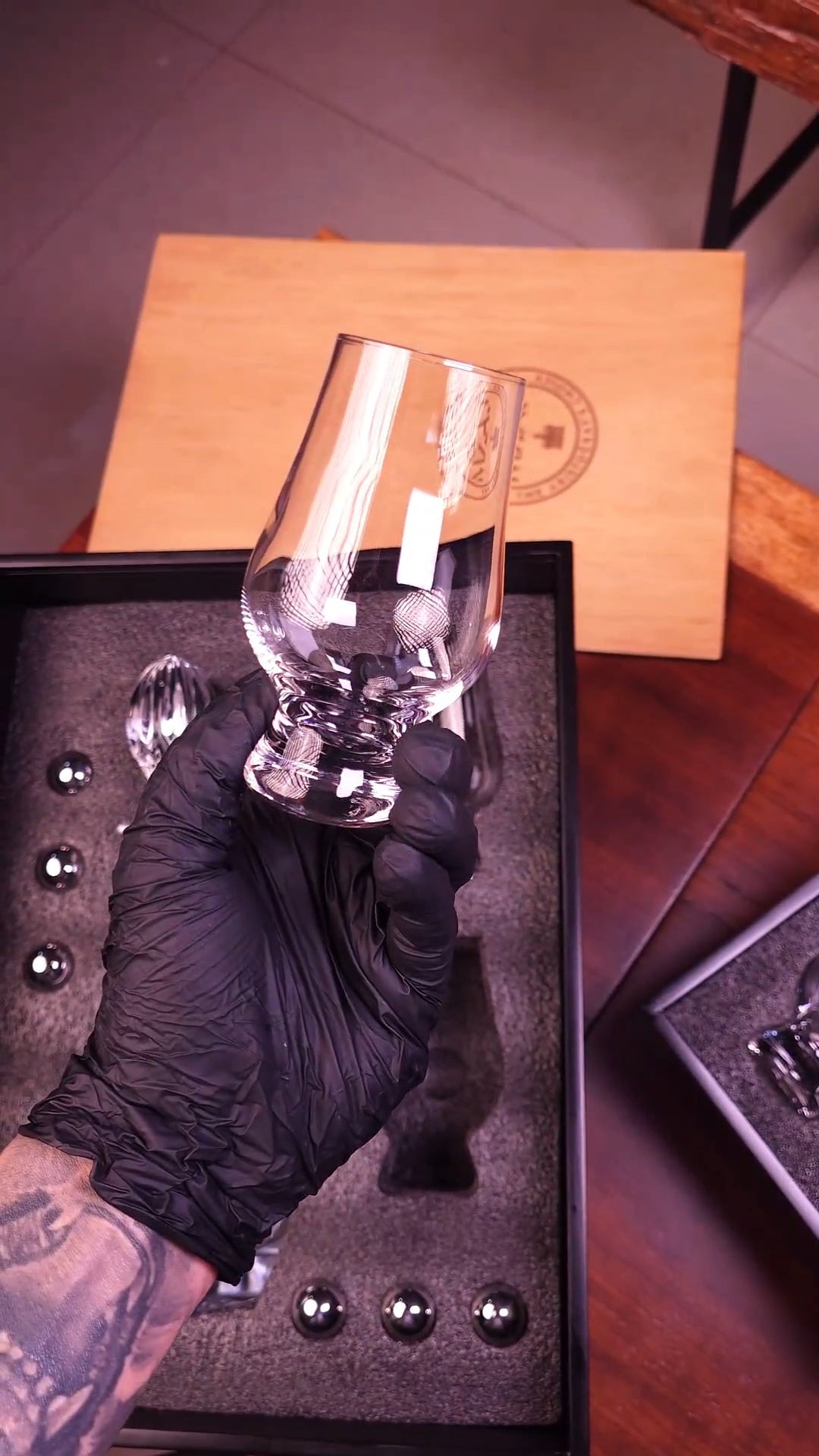 Clear glass object held by a gloved hand on a textured surface with a box in the background.