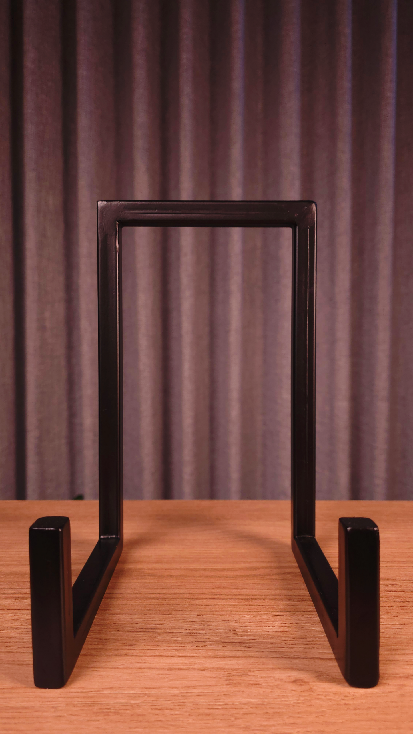 Black metal stand on a wooden surface with a dark gray curtain background