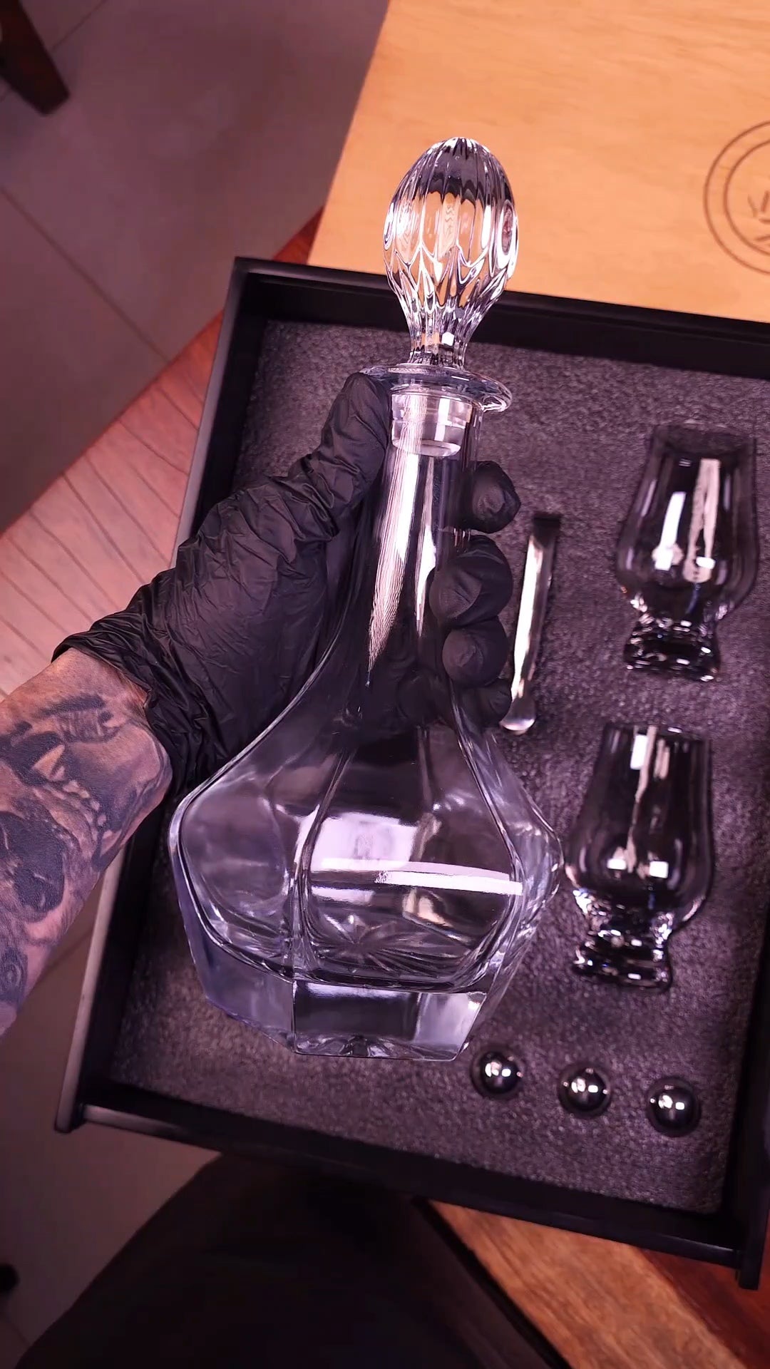 Clear glass decanter set with stopper and accessories on a black tray.