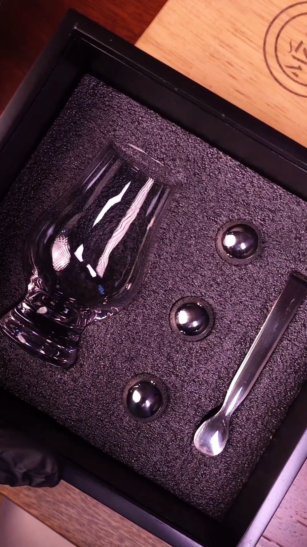 Glass set with three stainless ice stones and a tong in a black box on a wooden surface