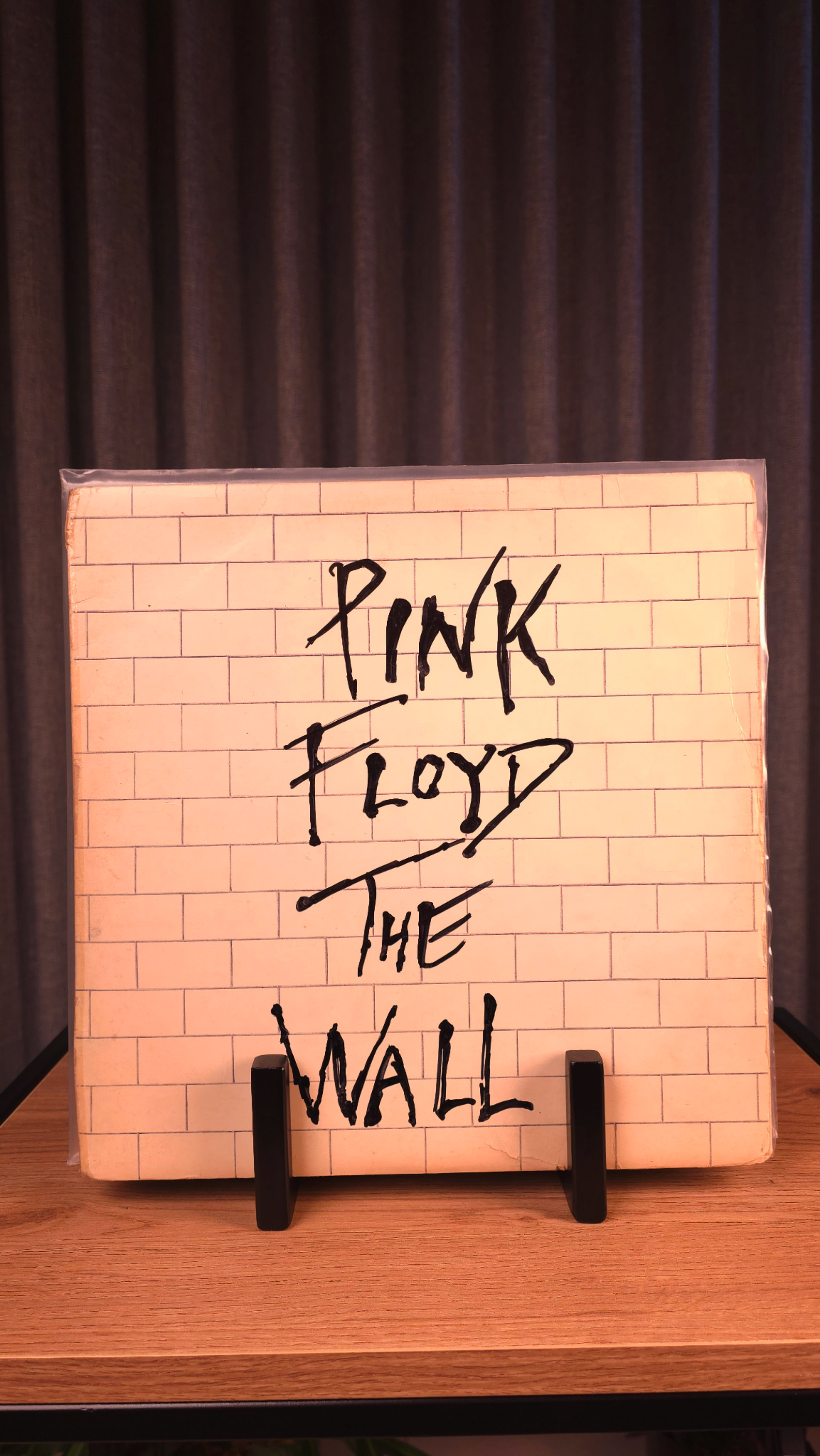 Album cover of 'The Wall' by Pink Floyd on a black metal vinyl stand with a dark gray curtain background