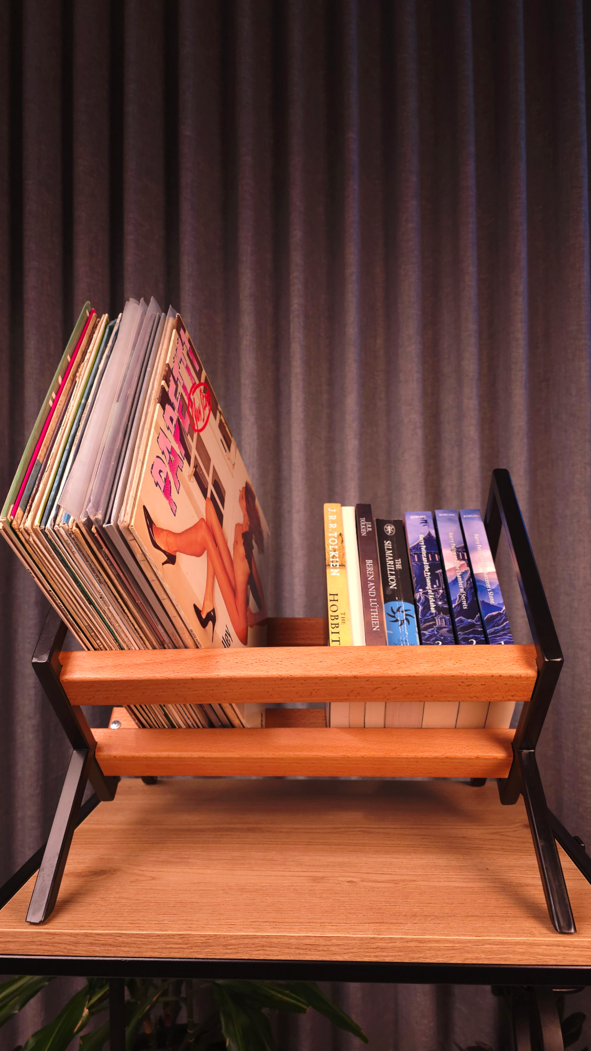 Wooden record player stand with vinyl records and books against a dark curtain background