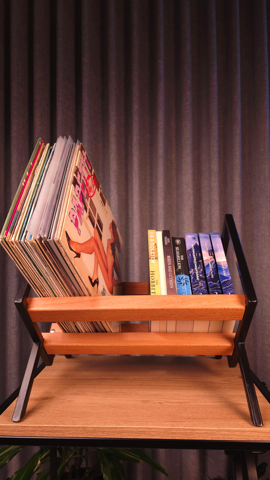 Wooden record player stand with vinyl records and books against a dark curtain background